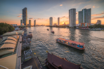 Chao Phraya River with Skyscrapers and Sathon Pier with Boats at Sunset as Seen from Taksin Bridge in Bangkok, Thailand