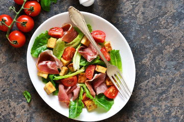 Salad with tomatoes, prosciutto and grilled cheese on a stone background.
