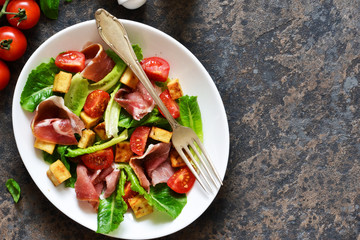 Salad with tomatoes, prosciutto and grilled cheese on a stone background.