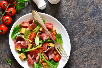 Salad with tomatoes, prosciutto and grilled cheese on a stone background.