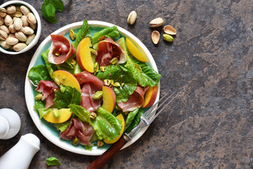 Fresh prosciut salad with peppers and pistachios on a concrete background. View from above.