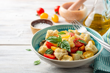 Traditional Italian salad Panzanella with cherry tomatoes, bread, capers and basil in bowl on wooden table. Selective focus.