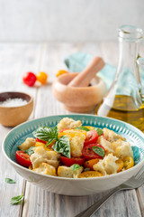 Traditional Italian salad Panzanella with cherry tomatoes, bread, capers and basil in bowl on wooden table. Selective focus.