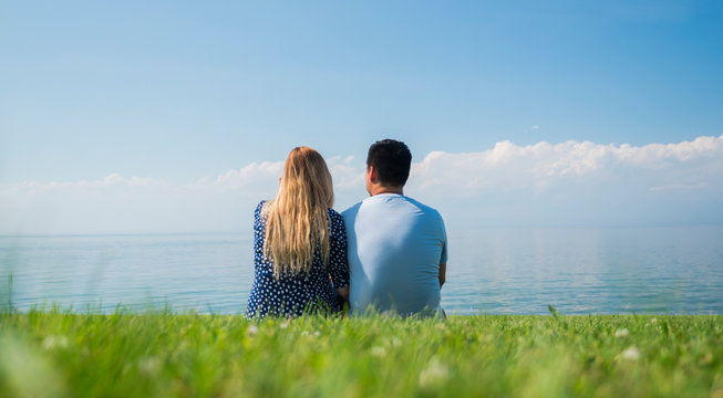 A young couple is sitting on a green lawn in a picturesque place near the lake