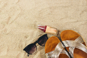 Fototapeta na wymiar Sunglasses and slippers, liquid foundation on sand, summer concept