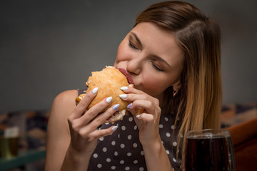 Young woman eating hamburger in restaurant. Close up face with closed eyes