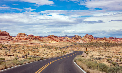 Long winding highway with ups and downs, cloudy blue sky. Valley of Fire Nevada, USA