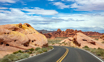 Long winding highway with ups and downs, cloudy blue sky. Valley of Fire Nevada, USA