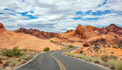 Long winding highway with ups and downs, cloudy blue sky. Valley of Fire Nevada, USA