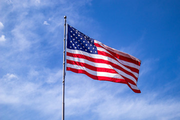 United States flag on a pole waving on blue sky background.