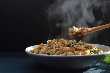 rice with spicy fried chicken Thai basil and vegetables smoke on it on a black background      