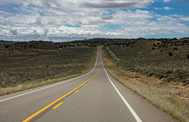 Fototapeta na wymiar Long highway in the american countryside, cloudy blue sky