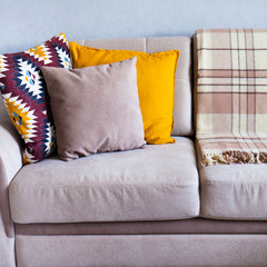 Cushions and plaid on the beige sofa close up with copy space. Sweet home and cozy concept