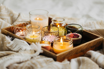 Burning candles on wooden tray with warm plaid in bed.  Scandinavian style. Hygge concept.