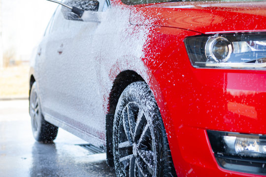 Black dirty car in white soap foam at car wash service station