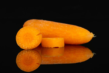 Fototapeta na wymiar Group of one whole two pieces of peeled orange baby cut carrot isolated on black glass