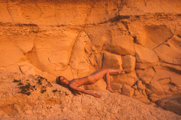 Young woman  lying on sand stone in lame dress