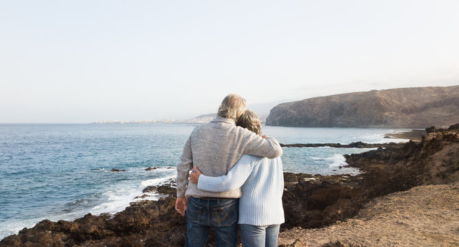 Caucasian couple of people with gray hair standing on the cliff of the ocean. Morning soon outdoor with clear sky. Vacation and happiness for pensioners