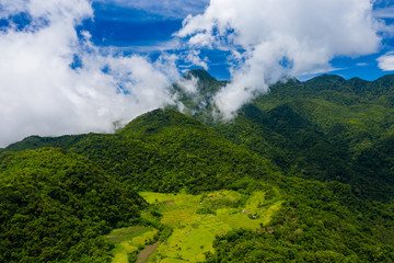 Aerial drone view of clouds passing over lush greenfarmland with mountains and volcanos in the background (Camiguin, Philippines)