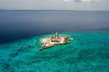 Aerial view of a tiny tropical island with a lighthouse surrounded by a huge coral reef...