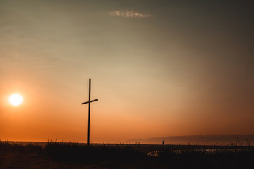 Fototapeta na wymiar Concept conceptual black cross religion symbol silhouette in grass over sunset or sunrise sky, Resurrection of Jesus, Cross christian