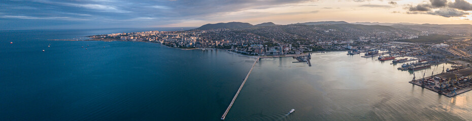 The sea city of the port of Novorossiysk from the height at sunset in regional weather where you can see the port gates, terminals and the pier.