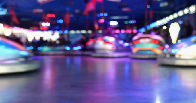 Low angle and defocus view of Illumination and motion of bumper cars. Blurry funny night atmosphere at typical  amusement park, carnival and fun fair.  