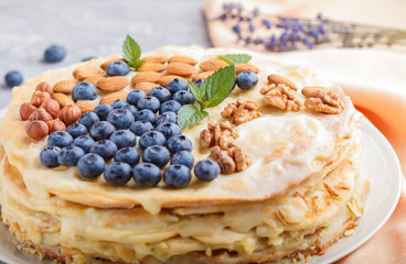 Homemade layered Napoleon cake with milk cream. Decorated with blueberry, almonds, walnuts, hazelnuts, mint on a gray concrete  background. side view.