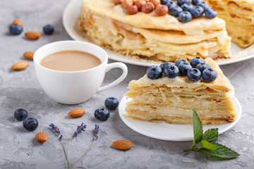 Homemade layered Napoleon cake with milk cream. Decorated with blueberry, almonds, walnuts, hazelnuts, mint on a gray concrete  background. side view, selective focus.