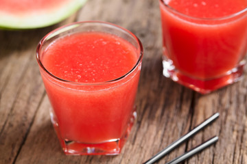 Refreshing watermelon juice on rustic wood (Selective Focus, Focus on the front of the glass rim)