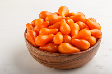 Fresh orange grape tomatoes in wooden bowl on white wooden background. side view.