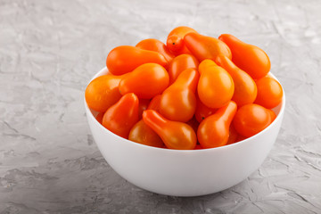 Fresh orange grape tomatoes in white ceramic bowl on gray concrete background. side view.