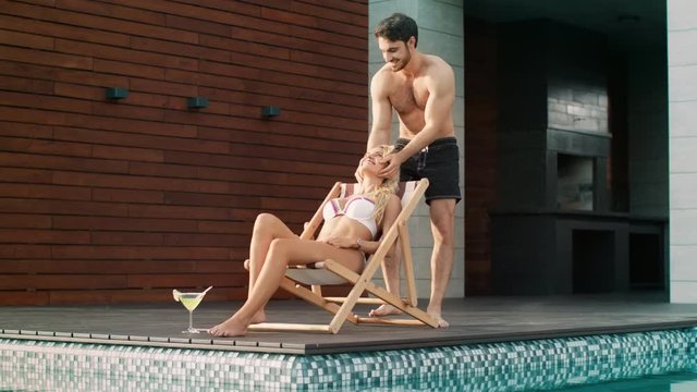 Athletic man kissing sexy woman near swimming pool at luxury house.
