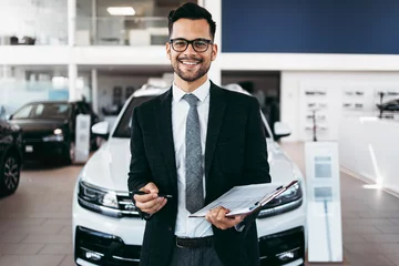 Foto op Canvas Good looking, cheerful and friendly salesman poses in a car salon or showroom. © Dusko