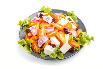 Vegetarian salad with fresh grape tomatoes, feta cheese, lettuce and onion on blue ceramic plate isolated on white background, side view.