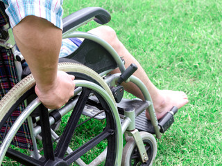 Obraz premium Paralyzed man using wheelchair during walk in park. He holds his hands on the wheel.