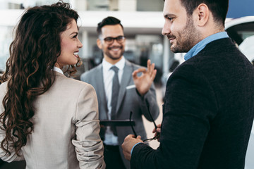 Middle age couple choosing and buying car at car showroom. Car salesman helps them to make right decision.