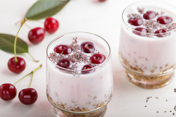 Yoghurt with cherries, chia seeds and granola in glass with wooden spoon on white wooden background. side  view.