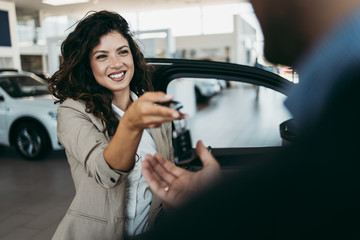 Happy middle age businessman buying new and expensive car. Beautiful female dealer gives him vehicle keys.