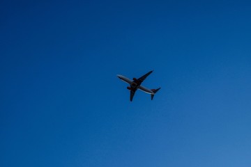 Airplane flying over business skyscrapers, high-rise buildings. Transport, transportation, travel. Sun light on blue sky.