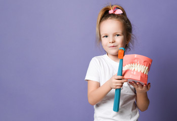 Happy girl kid and big dental implant model with toothbrush standing laughing on purple