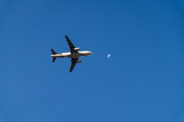 The plane is flying to the moon in the evening with the telecommunication wires in the frame