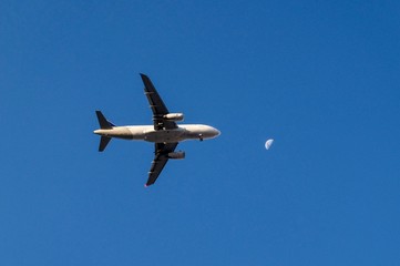 The plane is flying to the moon in the evening with the telecommunication wires in the frame