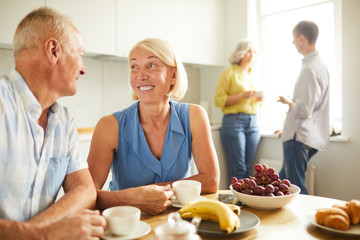 Portrait of happy adult couple looking at each other tenderly while siting at kitchen table in sunlight, copy space
