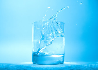 Refreshing glass of water, blue color ice cube dropping into glass