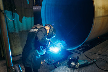 Worker in protective mask welding pipe in factory