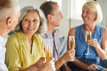 Group of modern senior people drinking champagne while enjoying party at home, copy space