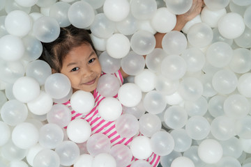 Fototapeta na wymiar Happy cute asian child girl having fun to play with white plastic balls in the playground