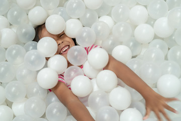 Happy cute asian child girl having fun to play with white plastic balls in the playground