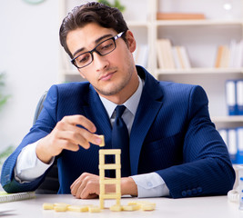 Young businessman building domino tower in office
